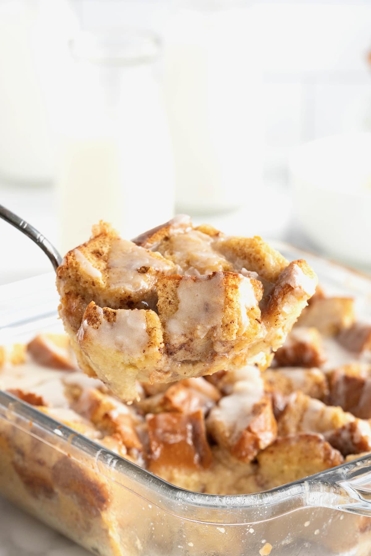 A bite of bread pudding on a fork held over a square glass baking dish of bread pudding. 